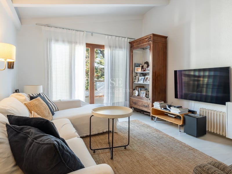 Salon lumineux avec canapés blancs, une grande armoire en bois, une télévision murale et un accès terrasse.