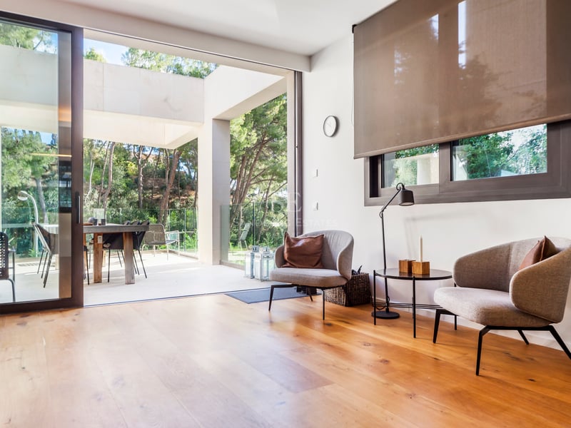 Coin salon moderne avec deux fauteuils gris sur parquet en chêne, s'ouvrant sur une terrasse ensoleillée.