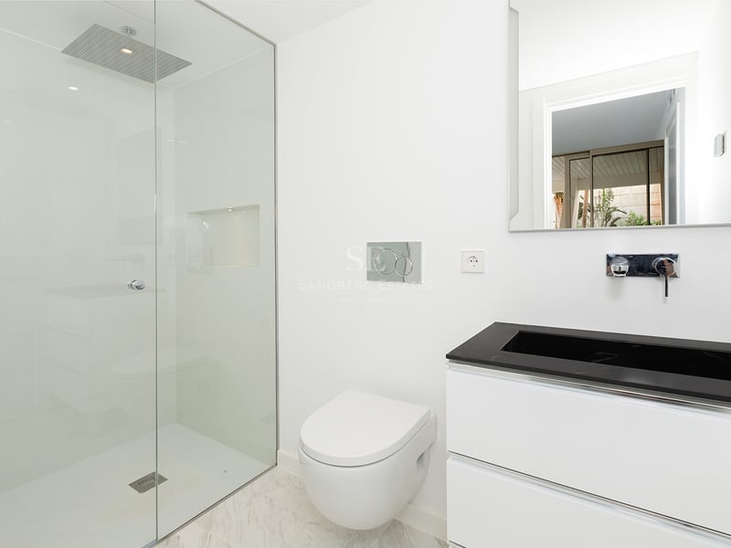 Salle de bain lumineuse et minimaliste avec douche en verre, toilettes suspendues et meuble vasque noir et blanc.