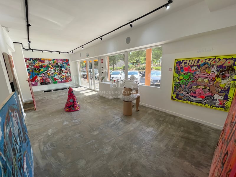 Une galerie d'art moderne avec des sols en béton, des murs blancs, des peintures contemporaines et une sculpture assise.