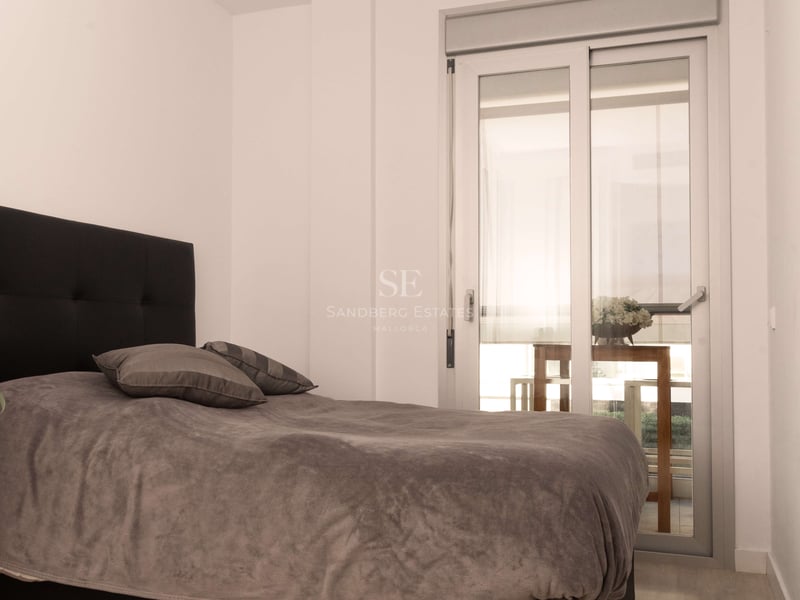 Chambre avec lit gris, tête de lit noire, parquet clair et porte vitrée coulissante menant à une terrasse.