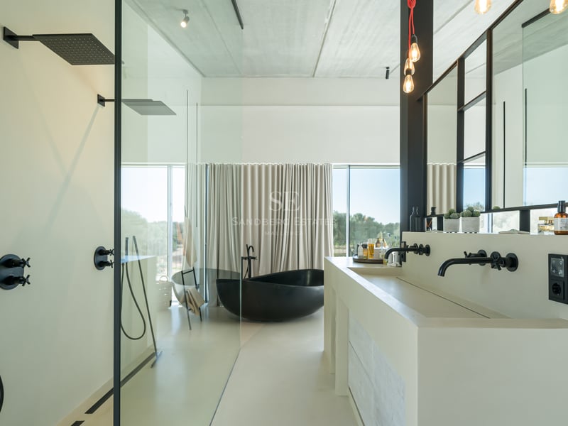 Salle de bains minimaliste avec baignoire îlot noire, double vasque blanche et grandes baies vitrées.