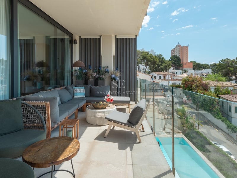 Vaste balcon moderne avec mobilier gris, garde-corps en verre et vue sur le quartier et la piscine au soleil.