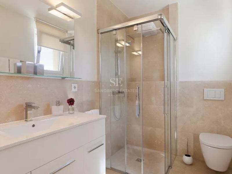 Salle de bain moderne avec douche vitrée, carrelage en marbre crème, meuble vasque blanc et WC suspendu.
