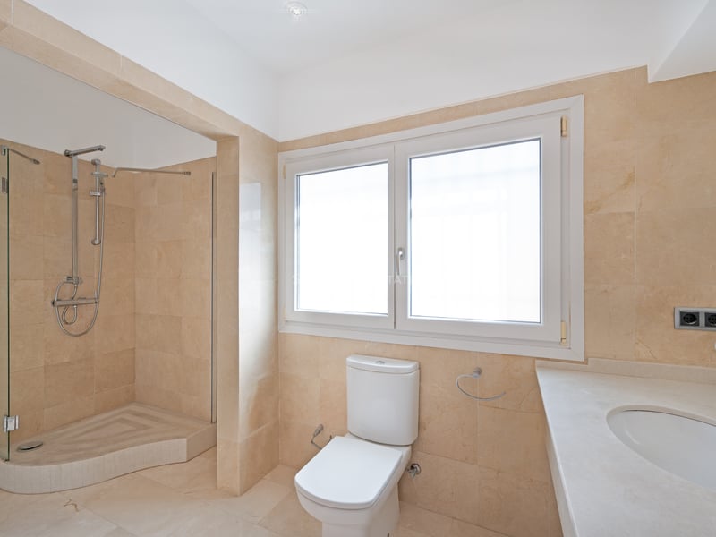 Salle de bain moderne avec murs en marbre crème, douche à l'italienne et grande fenêtre dépolie.