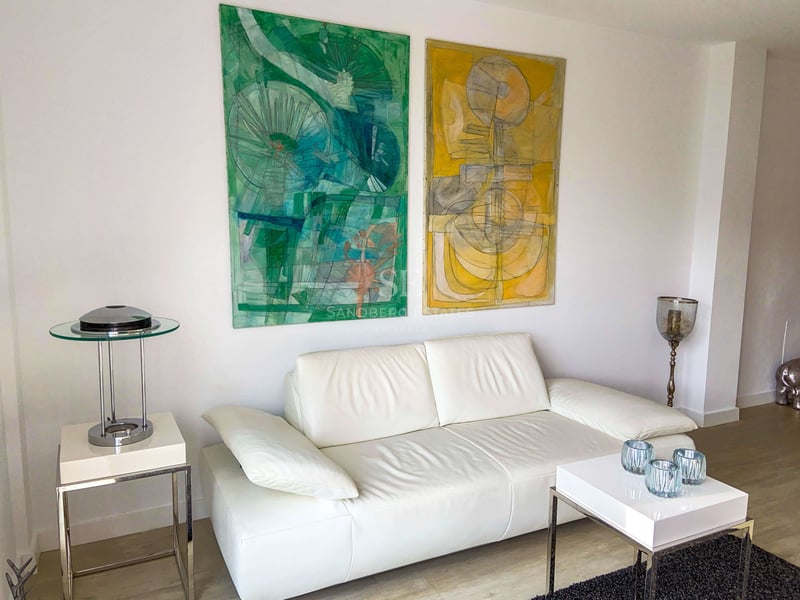 Canapé en cuir blanc avec peintures abstraites vertes et jaunes et mobilier minimaliste en chrome.