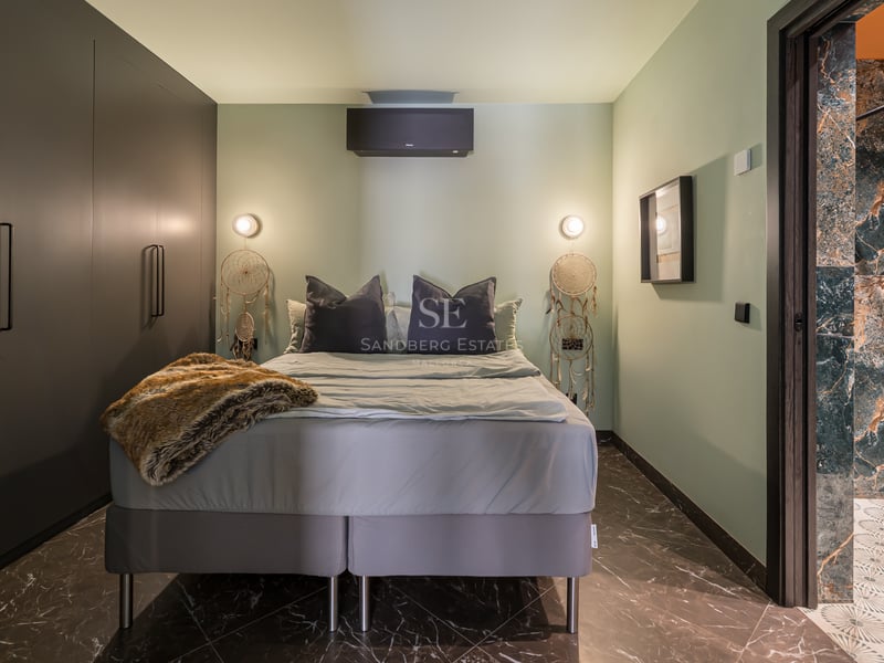 Chambre moderne avec murs vert sauge, sol en marbre sombre, placards intégrés et aperçu de la salle de bain attenante.