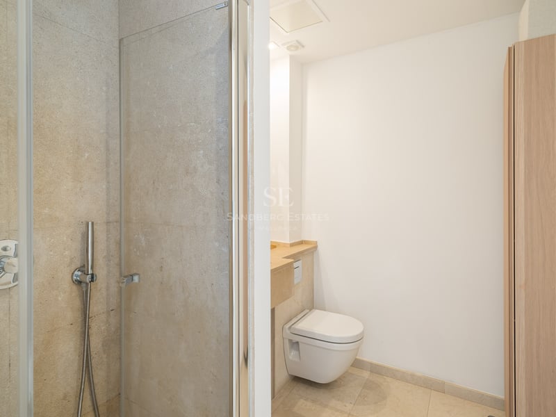 Salle de bain avec douche vitrée, toilettes suspendues et murs en pierre beige.