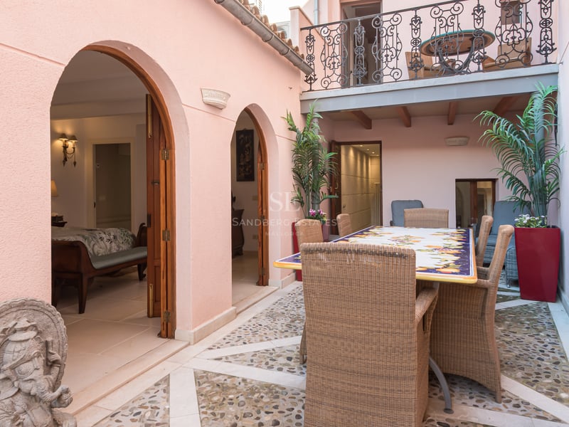 Patio privé avec sol en mosaïque de galets, mobilier en osier et murs roses aux arcades élégantes.