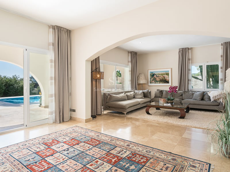 Grand salon moderne avec sol en marbre, canapés gris et baies vitrées ouvrant sur une piscine bleue.