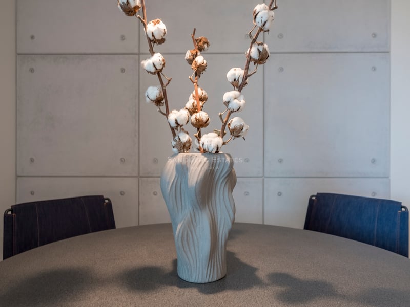 Vase gris texturé avec des branches de coton sur une table sombre devant un mur en panneaux de béton.