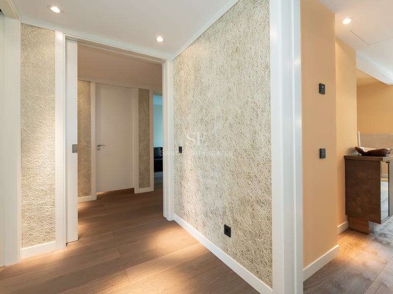 Couloir de luxe avec parquet en chêne, papier peint texturé et éclairage encastré menant aux pièces privées.