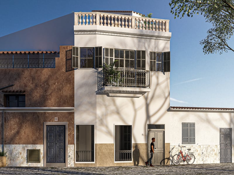 Dreistöckiges Gebäude in Weiß- und Ochtertönen mit mallorquinischen Fensterläden, Schmiedeeisenbalkonen und Dachterrasse.