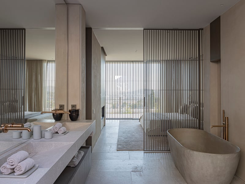 Salle de bain minimaliste avec baignoire en pierre, double vasque et laiton brossé, ouverte sur la chambre.