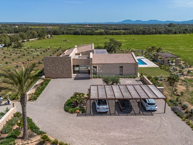 Vista aérea de una villa de piedra moderna con entrada de grava, pérgola y piscina frente al campo.