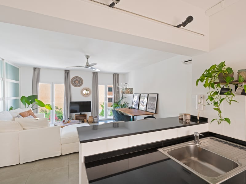Vue depuis le comptoir de cuisine vers un salon clair avec canapé blanc, coin repas et portes vitrées.