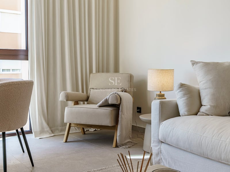Coin salon lumineux avec canapé crème, fauteuil, chaise bouclée et rideaux souples du sol au plafond.