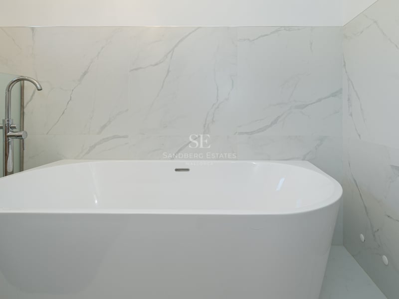 Baignoire îlot blanche avec robinetterie chromée sur fond de murs en marbre et sèche-serviettes.