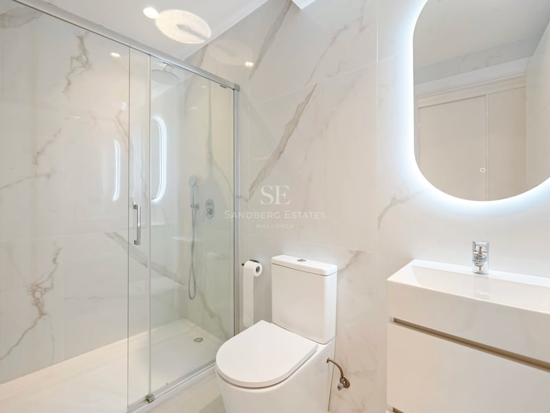 Salle de bains moderne avec murs effet marbre, douche à l'italienne vitrée et miroir ovale rétroéclairé.