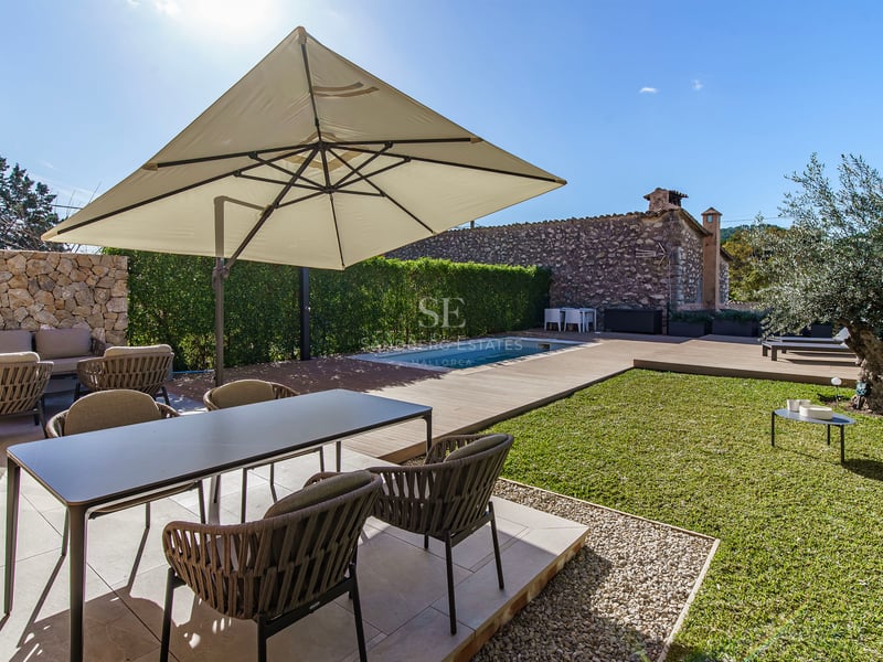 Terrasse ensoleillée avec salle à manger moderne, grand parasol, petite piscine et pelouse avec un olivier.