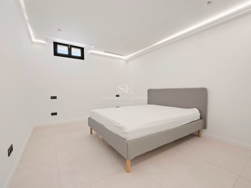 Chambre moderne avec lit tapissé gris, sol en grès cérame clair et corniche lumineuse LED au plafond.
