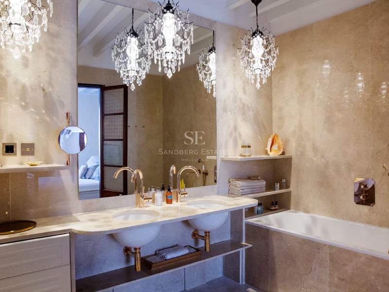 Cuarto de baño de lujo con dos lavabos, grifos de oro, paredes de mármol y tres lámparas de araña de cristal.
