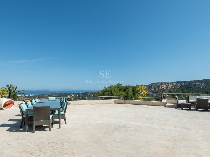 Terrasse en pierre avec coin repas et salon extérieur donnant sur la côte méditerranéenne et les collines.