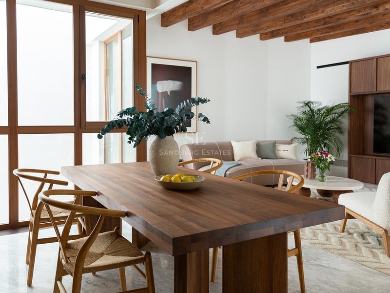 Comedor moderno con mesa de nogal, sillas de estilo Wishbone, vigas de madera vistas y suelos de mármol.