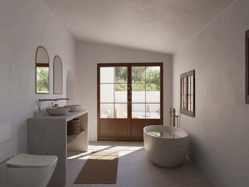 Salle de bains de luxe avec baignoire îlot, vasques en pierre et portes en bois ouvrant sur une terrasse ensoleillée.