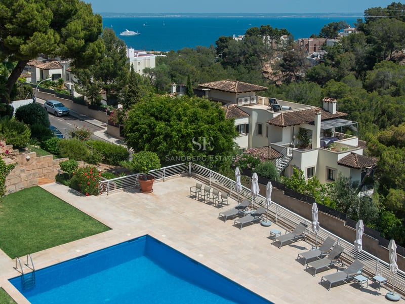 Vue aérienne d'une piscine bleue et terrasse avec chaises longues surplombant la Méditerranée et les villas.
