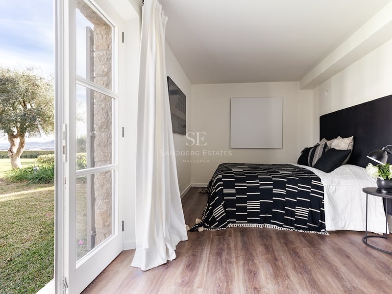 Chambre contemporaine avec parquet, lit double et grandes portes vitrées ouvrant sur un espace extérieur.