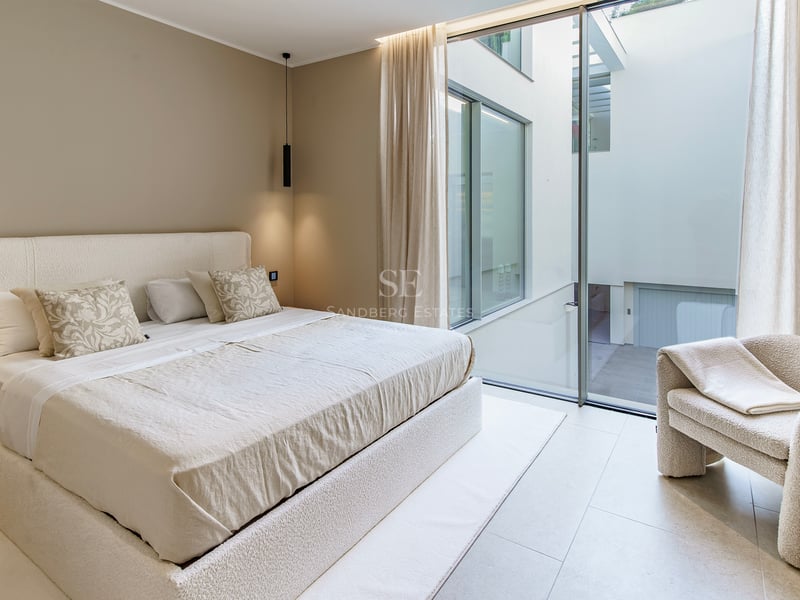 Chambre minimaliste avec lit en bouclé crème, fauteuil assorti et grandes baies vitrées donnant sur un patio intérieur.