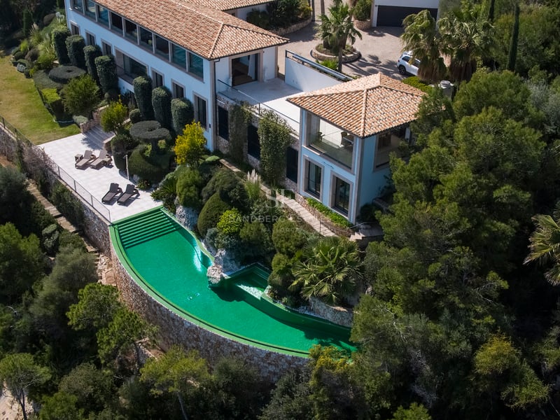 Vue aérienne d'une villa de luxe avec piscine à débordement émeraude, murs en pierre et toit en terre cuite.
