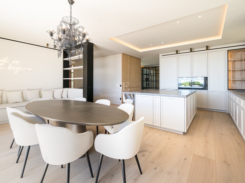 Une salle à manger spacieuse et moderne avec table ovale en bois, chaises blanches et cuisine intégrée.