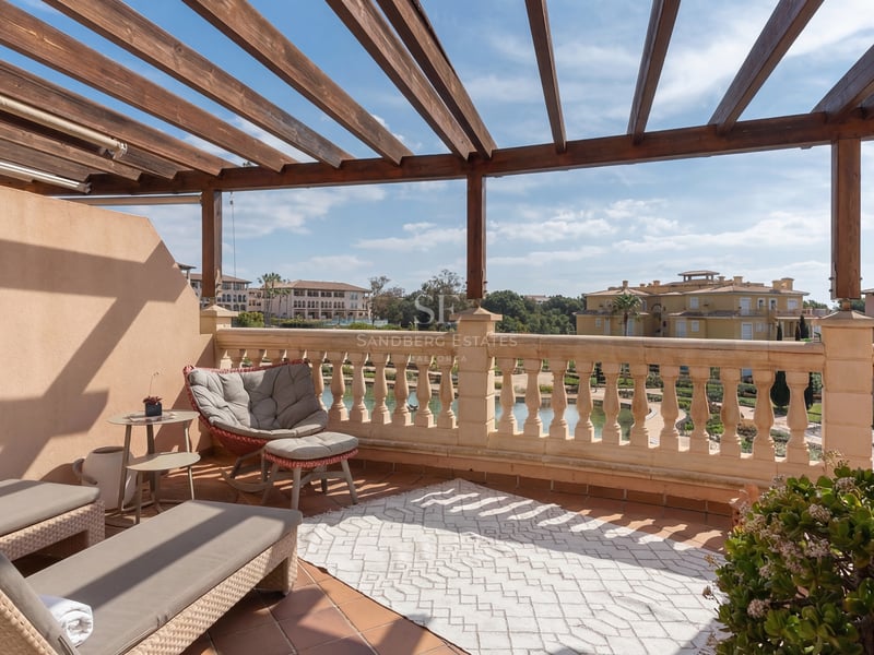 Terrasse privée ensoleillée avec pergola en bois, balustrade en pierre et coin salon donnant sur le quartier.