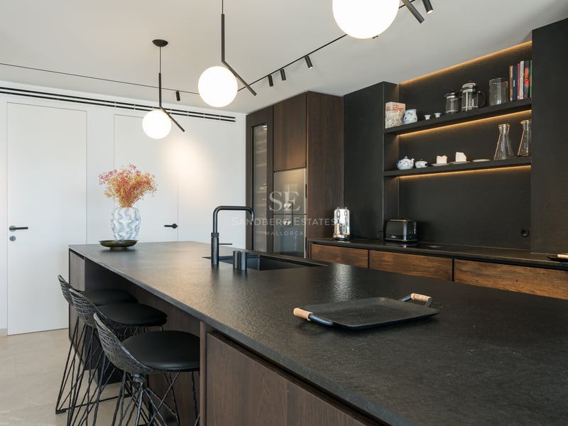 Cuisine contemporaine dotée d'un îlot en pierre noire, de placards en bois sombre et de suspensions sphériques.