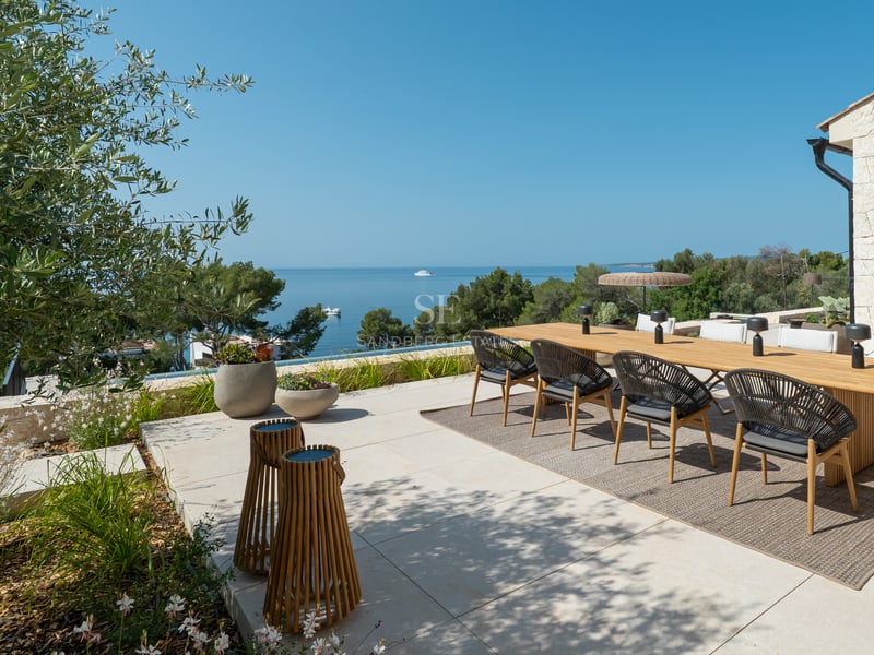 Grande table à manger en bois sur une terrasse en pierre naturelle offrant une vue panoramique sur la mer.