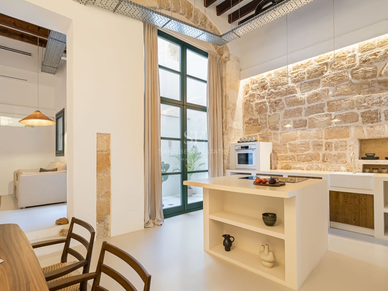 Cuisine moderne avec mur en pierre rustique, îlot blanc et poutres en bois au plafond.