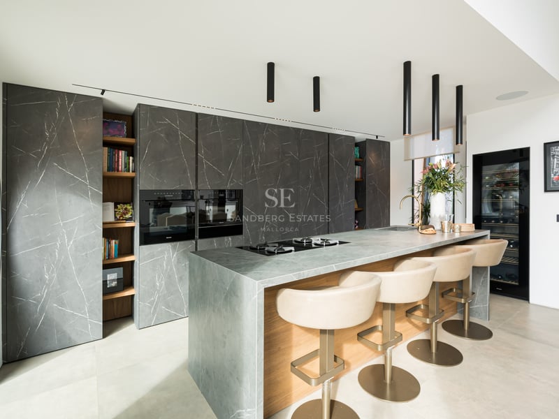 Cuisine moderne, placards marbre anthracite, îlot en pierre grise avec bar et suspensions design noires.