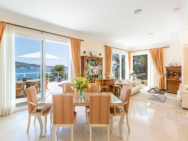 Salle à manger à aire ouverte avec table en verre, sol en marbre et grandes baies vitrées donnant sur la mer.