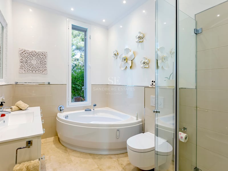 Salle de bains lumineuse avec baignoire balnéo, douche en verre, sol en marbre et vue sur le jardin.