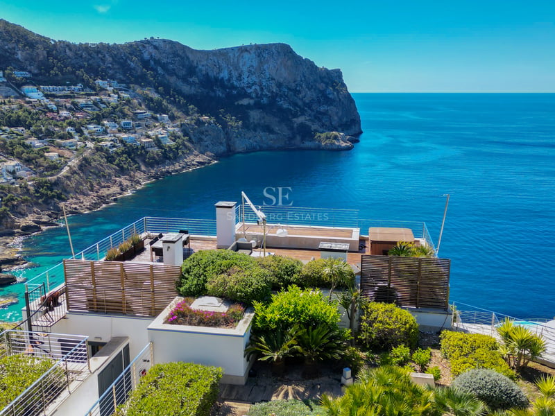 Terrasse contemporaine avec garde-corps en verre surplombant la mer et des falaises escarpées.