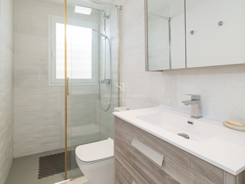 Salle de bain lumineuse avec meuble vasque en bois, grand miroir et douche vitrée.