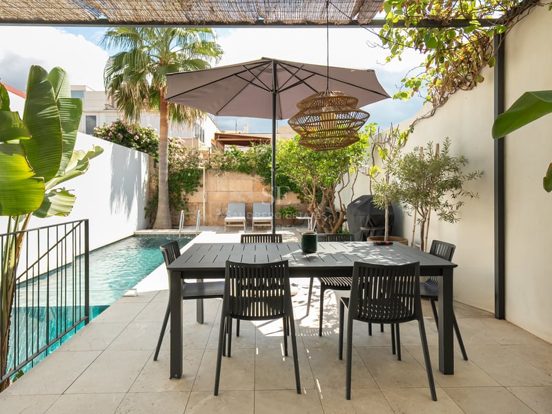 Terrasse moderne avec table à manger noire sous un parasol, à côté d'une piscine turquoise et de palmiers.