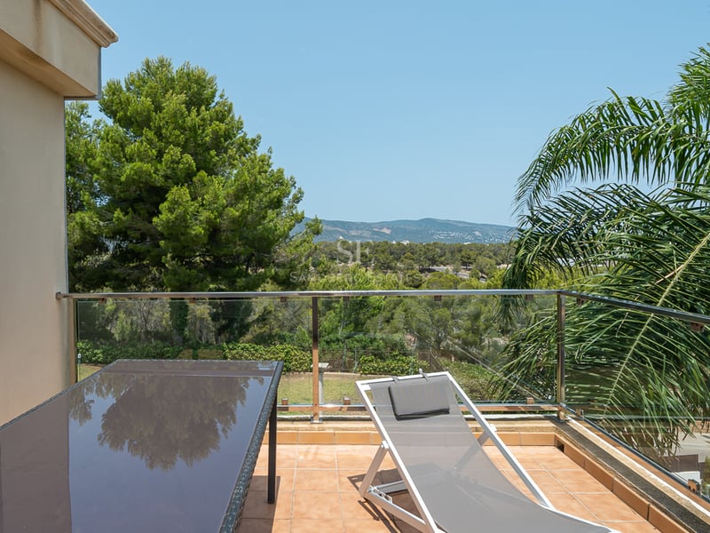Terrasse en terre cuite avec chaise longue et garde-corps en verre offrant une vue sur une forêt de pins.