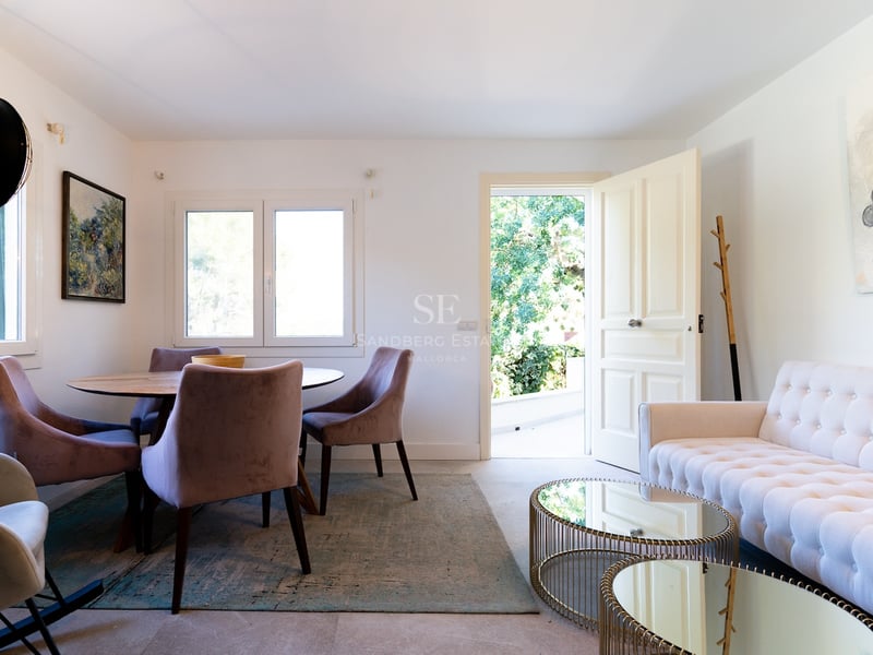 Salon lumineux avec canapé capitonné blanc, tables basses en miroir et coin repas avec chaises en velours.