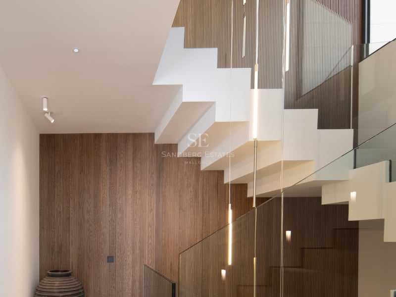 Escalier intérieur contemporain avec marches blanches, garde-corps en verre et panneaux muraux en bois vertical.