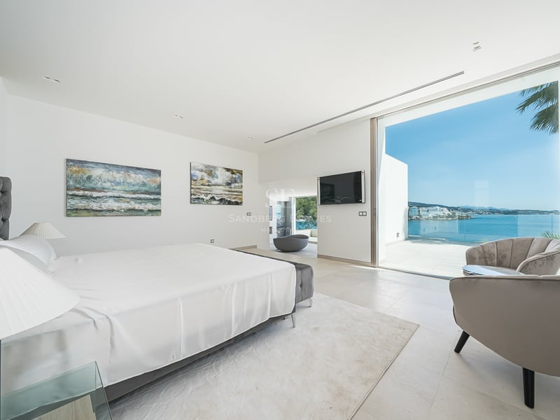 Chambre principale lumineuse avec literie blanche, fauteuils en velours et grandes baies vitrées donnant sur la mer.