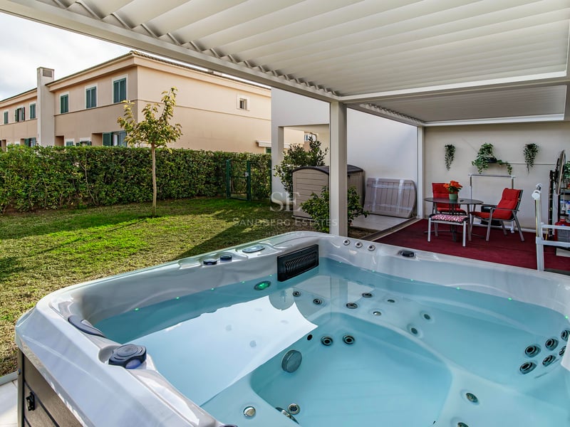 Jacuzzi de luxe blanc sous une pergola bioclimatique donnant sur un jardin privé avec des chaises rouges.