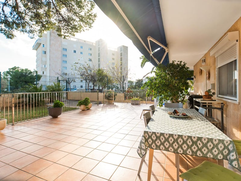 Vaste terrasse extérieure avec carrelage en terre cuite, table à manger sous un store et murs en pierre naturelle.